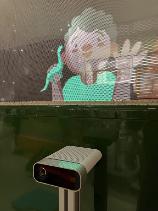 Bus Window with sensor in front. Window has a projected character, a little boy with a dinosaur toy.